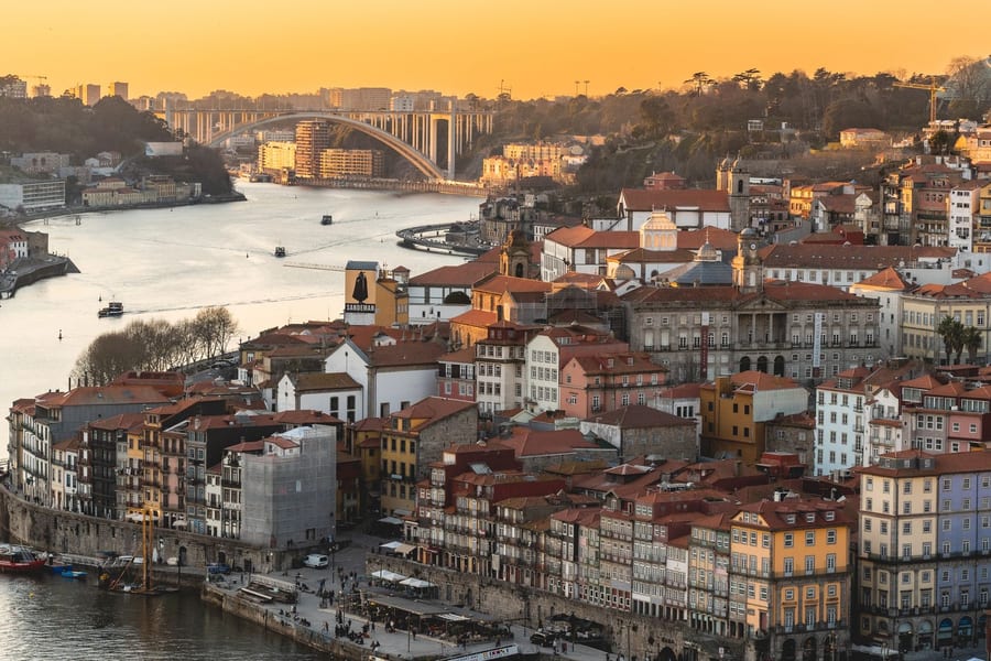 Vista do Porto e do rio Douro ao pôr do sol, com uma ponte ao fundo